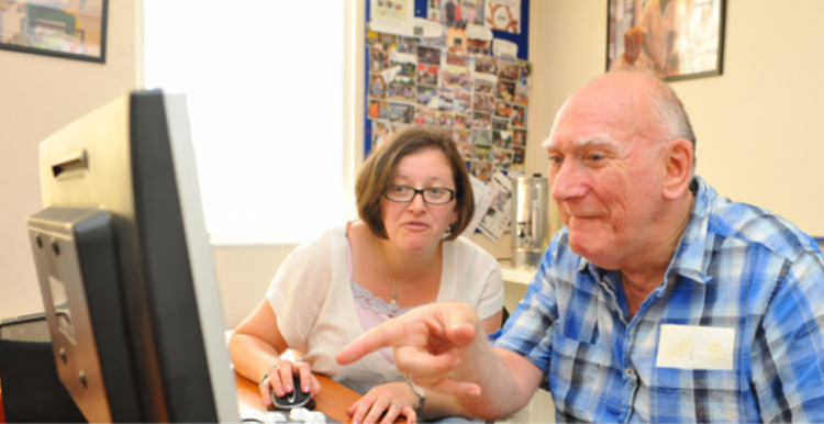 A woman showing a man with learning disabilities some information on a computer screen