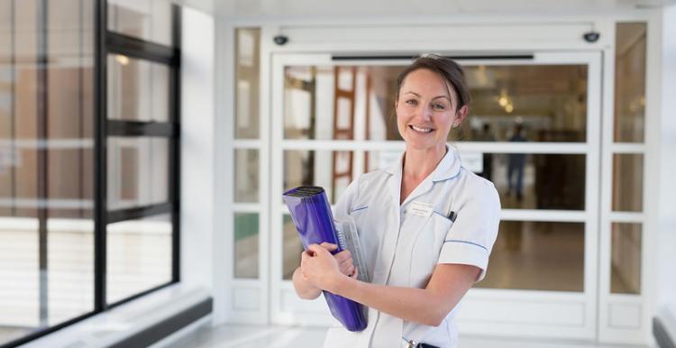 Smiling nurse with a clipboard in a hospital corridor