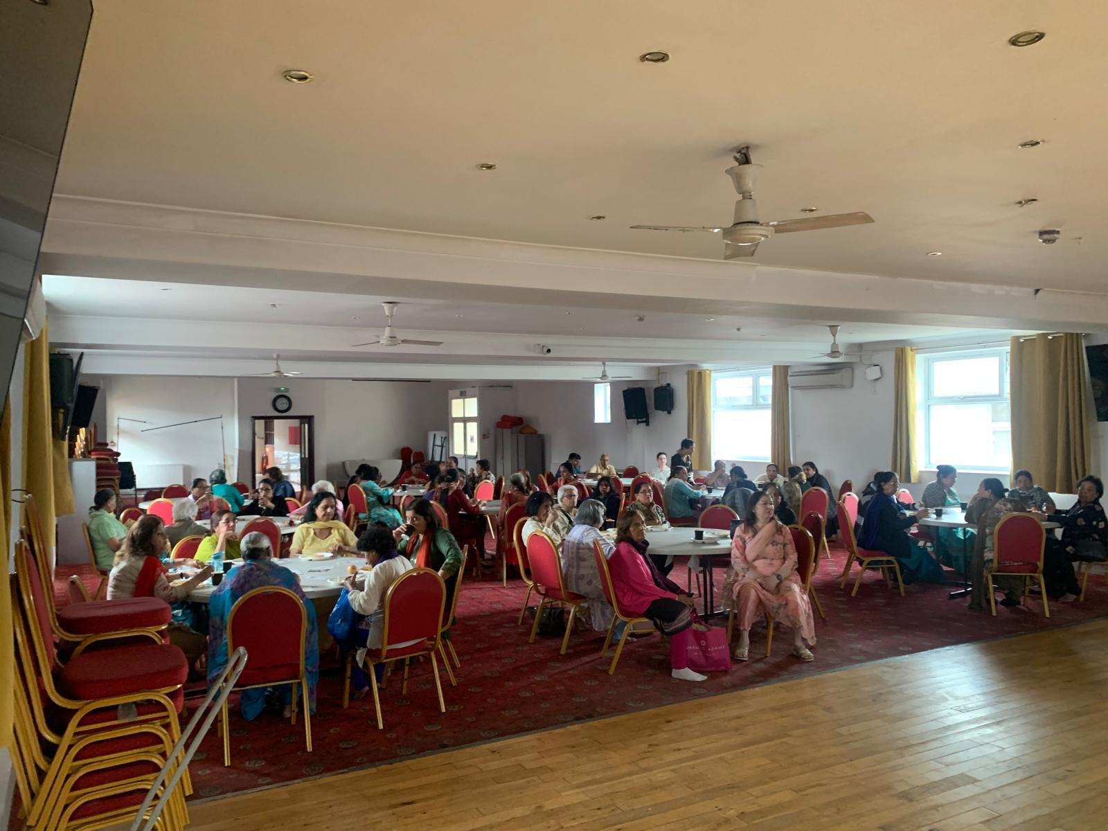 A photo of a large hall in a community centre full of people sat at round tables