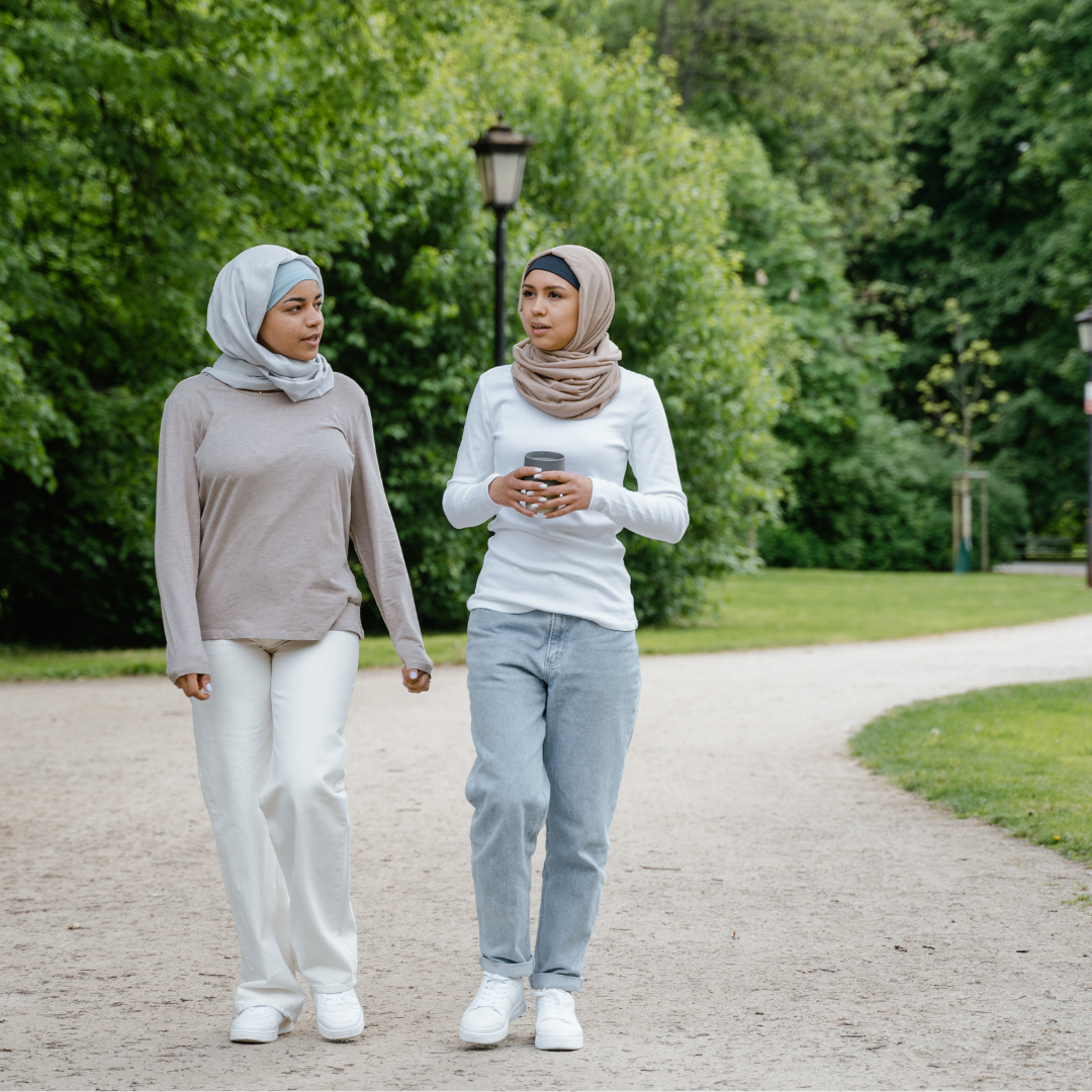 A photo of two women in hijabs walking through a park in exercise clothes