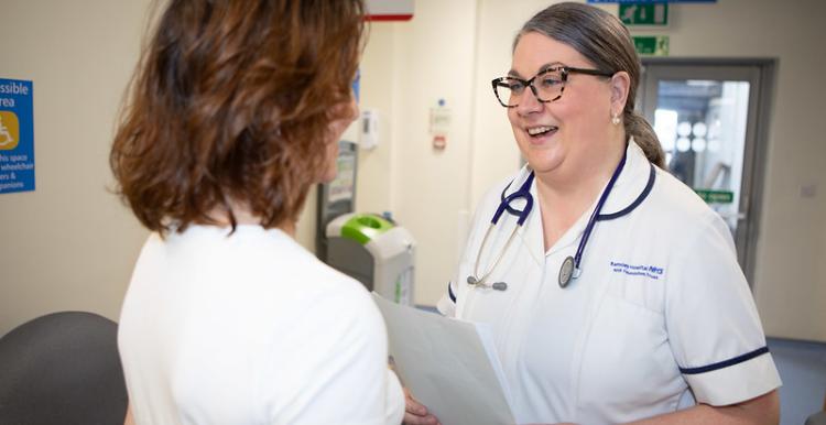 A woman talks to a NHS staff member in a hospital waiting room