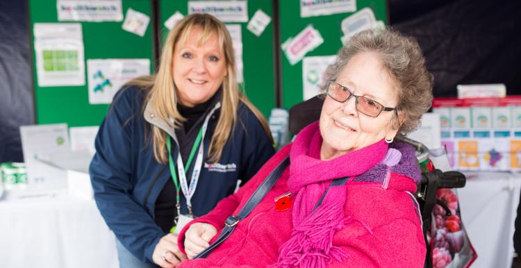 Healthwatch Volunteer at a community event speaking to a woman in a wheelchair