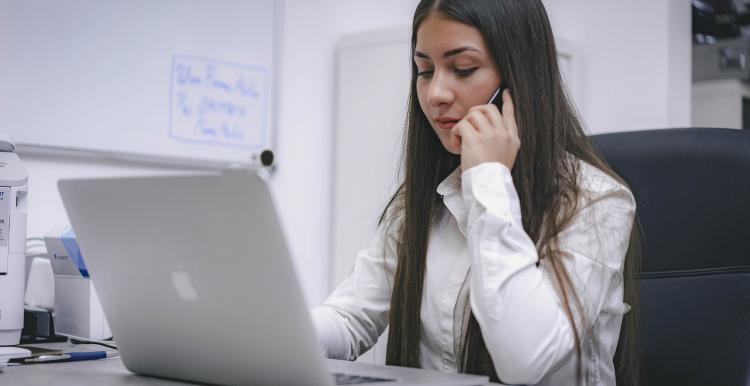 A young lady looking at her laptop whilst making a mobile call