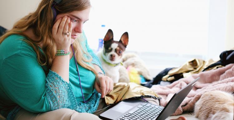 A young woman sat on her bed with her laptop