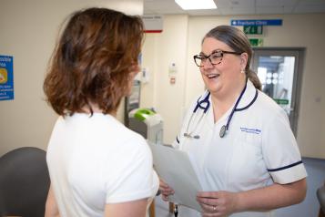 A woman talks to a NHS staff member in a hospital waiting room