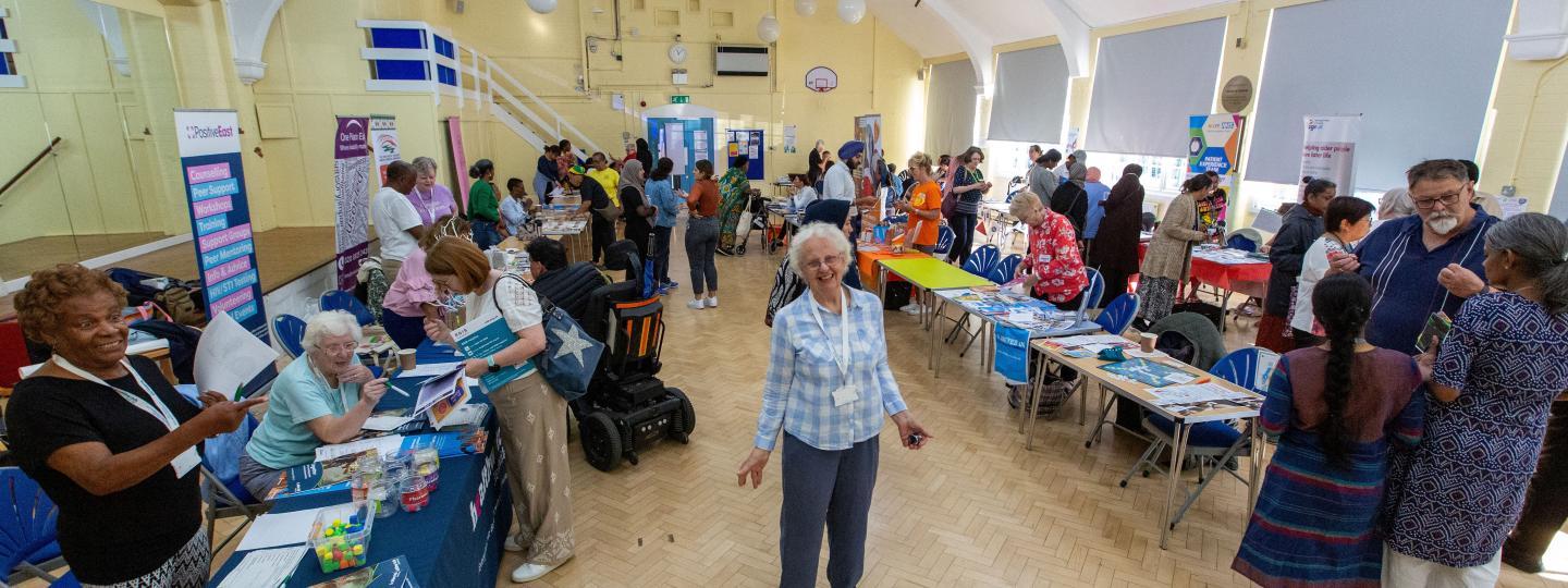 Image of woman standing with open arms in a room full of people engaging at stalls