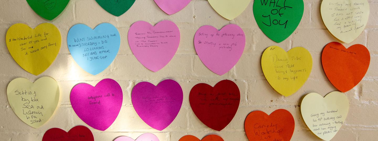 A photo of paper hearts with hand written messages on a wall